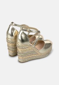 Goldene metallische Wedge-Sandalen mit überkreuzten Riemen, gewebtem Jute-Plateau und strukturierten geflochtenen Akzenten. Verstellbare Knöchel-Schnalle für einen sicheren Sitz.