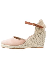 Blush pink suede wedge sandal with a braided jute platform, featuring a brown ankle strap with a buckle and an open toe design.