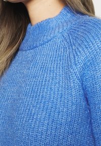 Pull tricoté bleu clair avec un col rond. Motif côtelé texturé et tissu légèrement transparent. Vue rapprochée des détails de la couture.