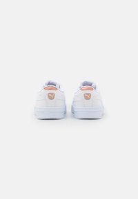White athletic shoes with a smooth leather upper, textured accents, and a light pink logo on the heel. Low-top design with padded collar.