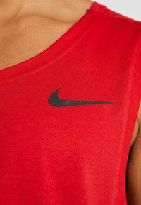 Close-up af en person iført en rød ærmeløs sportstrøje med en sort Nike-logo på brystet.