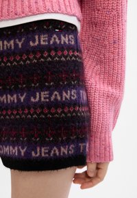 Roza pletena vestu uparenjena s pletenim ljubičastim i crnim šortsevima koji imaju ponavljajući dizajn teksta "Tommy Jeans" i geometrijske uzorke.