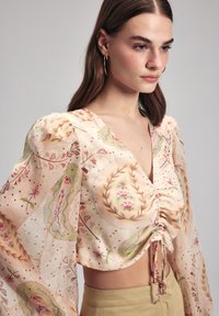 Leichte, durchsichtige Bluse in einem pastellfarbenen Blumenmuster mit gerafftem Vorderteil und voluminösen Ärmeln. Verfügt über eine Kordelzugdetails und dezente Punkte.