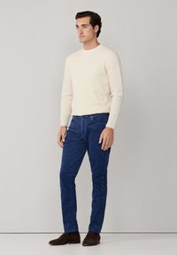 Suéter crema de punto trenzado, pantalones azules y zapatos marrones. El suéter presenta patrones texturizados, mientras que los pantalones son suaves y tienen una silueta ajustada.