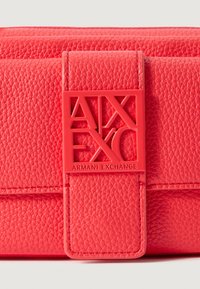 Torebka syntetyczna o fakturze koralowej w kształcie prostokąta. Posiada wyraźny czerwony plastikowy zamek z logo "Armani Exchange".