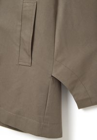 Light brown fabric jacket featuring a side pocket, subtle stitching detail, and a relaxed fit with a curved hem. Smooth texture.