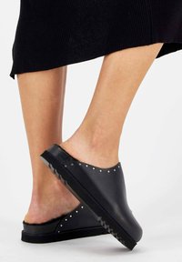 Black slip-on shoes with a smooth leather upper, furry lining, and studded accents along the edge. Textured rubber outsole for grip.