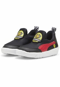 Fekete szövet slip-on sportcipők piros részletekkel, fehér talppal, kockás húzófülekkel és sárga-fekete mesefigurás logókkal.