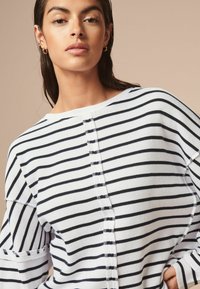 Maglione a righe in maglia con strisce orizzontali bianche e blu scuro, scollatura a barca e dettagli con bottoni lungo la parte anteriore e le maniche.