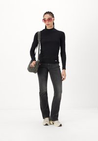 Black long-sleeve top, gray jeans, beige sneakers. Model holds a gray shoulder bag and wears oversized pink sunglasses. White background.