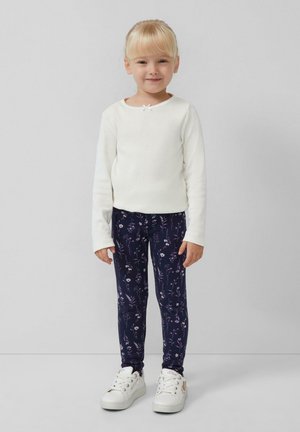Top bianco a maniche lunghe con scollo rotondo e un piccolo fiocco. Leggings blu navy con motivo floreale. Sneakers bianche con lacci e dettagli.
