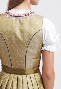 Femme portant une robe verte à motif floral avec une ceinture marron et un chemisier blanc à manches bouffantes avec bordure en dentelle.