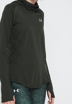 Osoba nosící tmavě zelenou mikinu s dlouhým rukávem značky Under Armour a černo-zelené legíny s vzorem a otevíracími otvory na palce na rukávech.