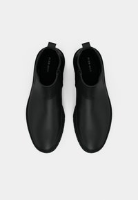 Zapatos formales de cuero negro tipo mocasín con punteras redondeadas y tiradores, vistos desde arriba sobre un fondo blanco liso.