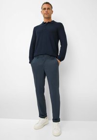 Polo shirt a maniche lunghe blu navy abbinato a pantaloni grigio scuro. Il modello indossa sneakers bianche. Design semplice; texture liscia, stile aderente.