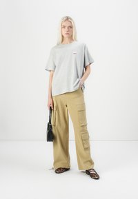 Gray cotton oversized t-shirt with a graphic print, paired with beige cargo pants featuring multiple pockets. Black handbag and leopard print shoes.