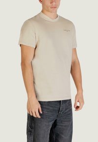 Beiges Baumwoll-T-Shirt mit kurzen Ärmeln und rundem Ausschnitt, mit kleinem aufgedrucktem Logo auf der Brust und einem lockeren Schnitt.