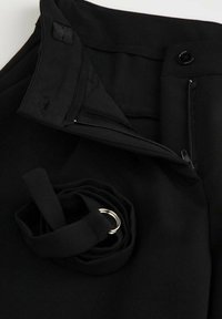 Czarne spodnie z rozpiętym zamkiem, z zapięciem w pasie oraz zwiniętym paskiem z materiału z srebrną podwójną klamrą.