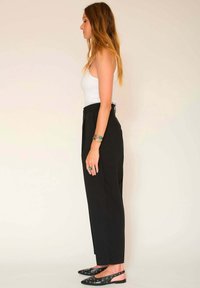 Pantalons noirs taille haute avec une coupe droite, associés à un débardeur blanc. Comprend des accents décoratifs en argent sur les chaussures et les bijoux.