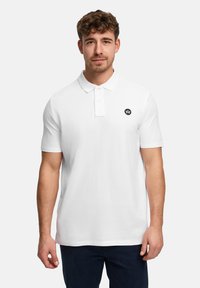 Hvid poloshirt med klassisk krave, korte ærmer og et sort logo på venstre bryst. Materialet virker glat med en bomuldsblanding.