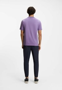 Violetti lyhythihainen paita pyöreällä pääntiellä, yhdistetty tummansinisiin kapealahkeisiin housuihin ja mustiin kenkiin, joissa valkoiset pohjat. Sileä pinta, minimalistinen muotoilu.