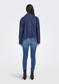 Jeansjakke i mørkeblå, med klassisk krage, cropped design og synlig søm. Brukt over blå skinny jeans og svarte ankelstøvler.