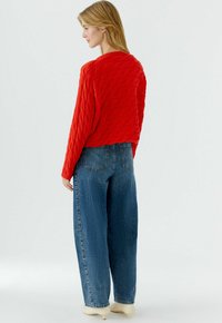 Roter Strickpullover mit langen Ärmeln und kurz geschnittenem Design, kombiniert mit hoch taillierten blauen Jeans aus Denim. Glatte Textur und lockere Passform.