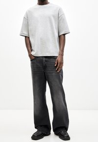 Sudadera gris de manga corta, de corte relajado; combinada con pantalones vaqueros de pierna ancha gris oscuro y zapatos negros con un acabado liso.