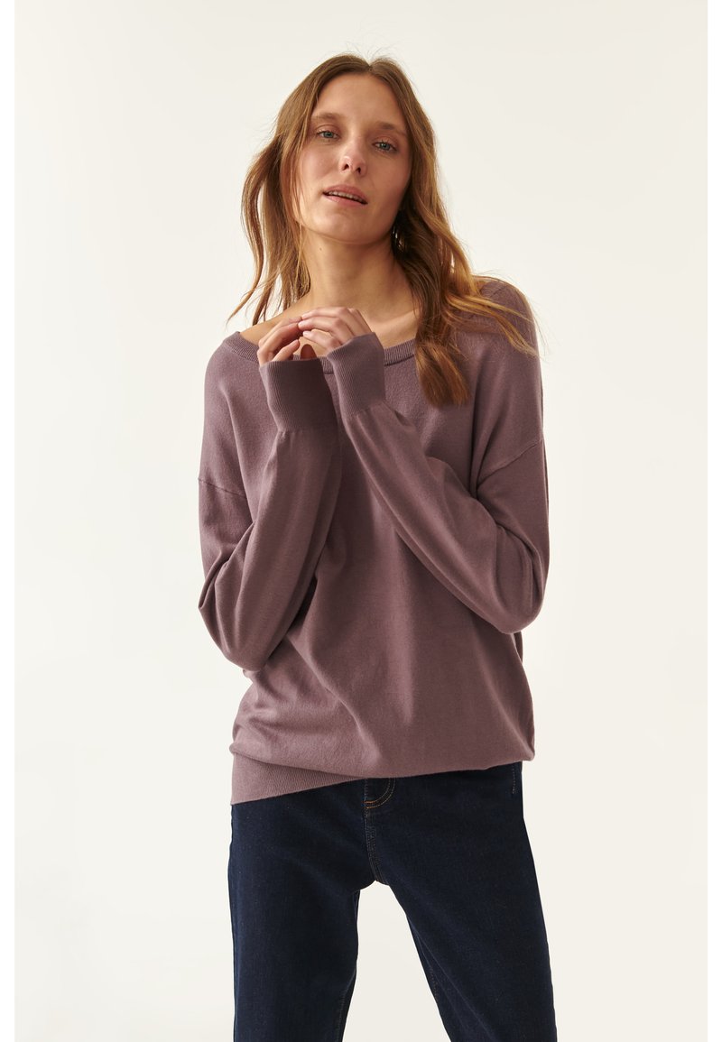 Pullover in mauve, con maniche lunghe, scollatura ampia e polsini a coste. Abbinato a jeans in denim scuro. Tessuto morbido.