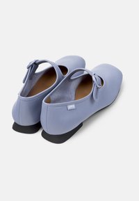 Ljusblå ballerina skor med ankelremmar och en liten svart klack, med en dekorativ rosett och Camper-logotypen på sidan.