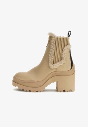 Bottine à talons beige avec un dessus texturé, des détails nervurés, une bordure en fourrure et une semelle en caoutchouc épaisse avec des motifs de traction.