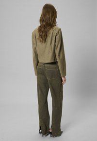 Olivengrøn cropped jakke med en struktureret finish, parret med matchende viddejeans med rå kant og baglommer.