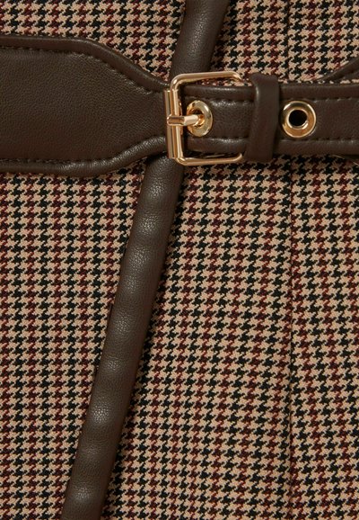 Primo piano di un tessuto intrecciato in un motivo a pied de poule con una tracolla in pelle marrone e fibbia dorata, che mostra dettagli di texture e colori.