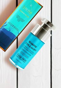 Serum z kolagenem morskim w przezroczystej niebieskiej butelce z srebrną nakrętką pompy. Opakowanie ma gradient niebieskiego z złotymi akcentami i logo marki.