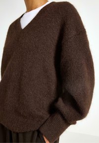 Maglione marrone a scollo a V realizzato in materiale morbido e peloso; presenta spalle cadute e polsini a costine. Design semplice senza motivi visibili.