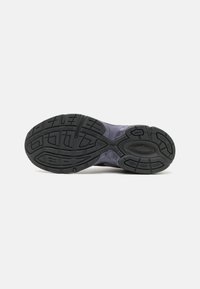 Semelle d'une chaussure de sport montrant un profil en caoutchouc noir texturé avec des rainures et motifs pour une bonne adhérence sur fond clair.
