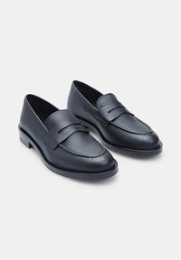 Loafers negri din piele cu un design cusut, o curea în față și un toc mic pe bloc. Textură netedă și formă clasică.