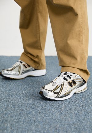 Baskets New Balance blanches et argentées avec des accents et des lacets noirs, dotées d'un dessus en maille, d'une semelle rembourrée et d'un design dynamique.