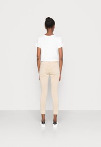 Camiseta blanca de manga corta, jeans skinny beige y zapatillas blancas con detalles negros. Fondo liso; enfoque en los detalles del atuendo.