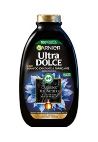 Flacone di shampoo in plastica nera con un cappuccio dorato, decorato con disegni floreali blu e un'etichetta nera che riporta la dicitura "Carbone Magnetico." Realizzato con materiali 100% riciclati.