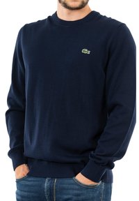Suéter de cuello redondo en azul marino, hecho de material suave, con puños y dobladillo acanalados, y un pequeño logo verde de Lacoste en el pecho.