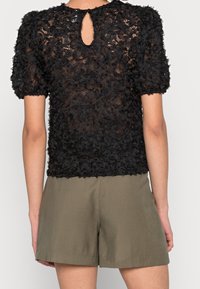 Haut en dentelle florale noire avec des manches bouffantes courtes. Détail en forme de clé au dos. Assorti à un short vert olive, mettant en valeur un tissu lisse et léger.