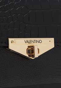 Borsa a tracolla in pelle nera con texture effetto coccodrillo, dotata di una chiusura in metallo dorato con inciso "Valentino" su una placca triangolare.
