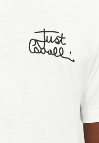 Tricou alb din bumbac, cu text brodat negru "Just Cathell" pe zona stângă a pieptului. Textură fină, mâneci scurte.