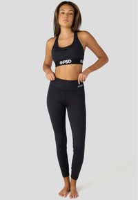 Svart träningsset som har en åtsittande sportbh och högmidjade leggings. Tillverkat av elastiskt material med en mjuk yta och logotyper.