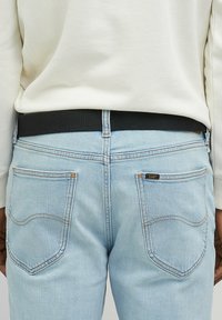 Lysblå denimjeans med slim fit, der har en sort elastisk talje, orange syninger og et lille "Lee" logo på baglommen.