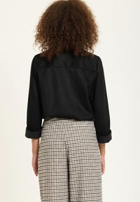 Black long-sleeved shirt with rolled cuffs, paired with high-waisted plaid trousers featuring a checkered pattern in black and white.