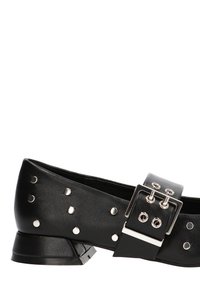 Zapato bajo de cuero negro con tachuelas plateadas y una correa ancha que presenta una gran hebilla cuadrada plateada.