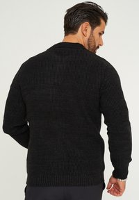 Schwarzer gestrickter Pullover mit geripptem Muster, langen Ärmeln und rundem Ausschnitt. Mit einem lockeren Schnitt und seitlichen Schlitzen am Saum.