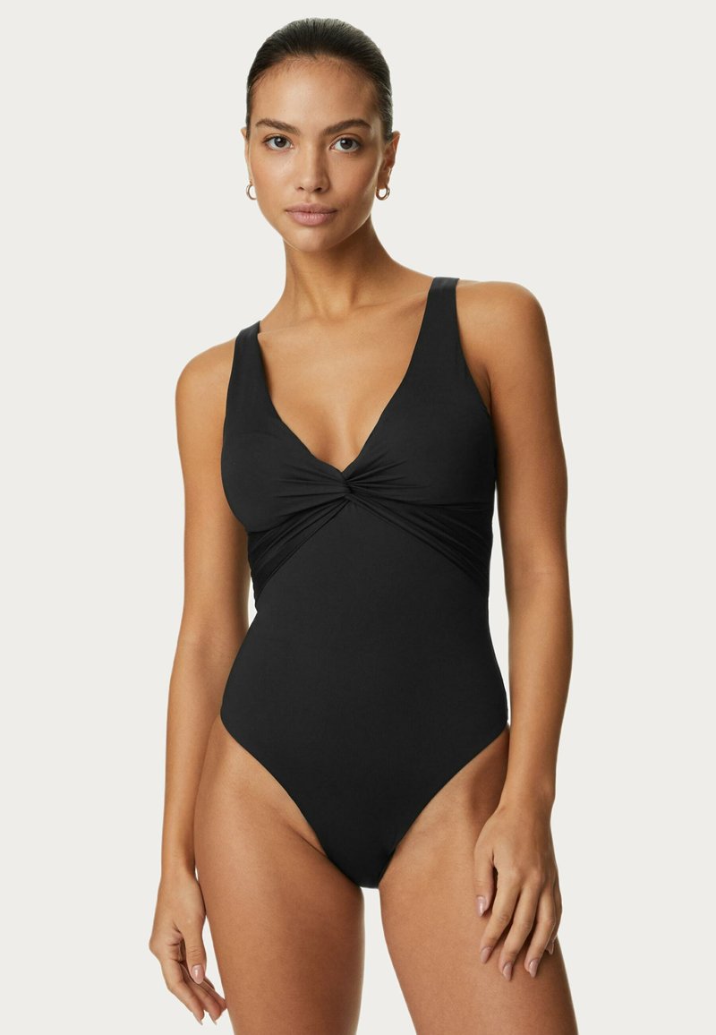 Maillot de bain noir une pièce avec un décolleté en V profond, un détail torsadé à l'avant, des bretelles larges et des découpes hautes sur les jambes, fabriqué à partir d'un tissu lisse.